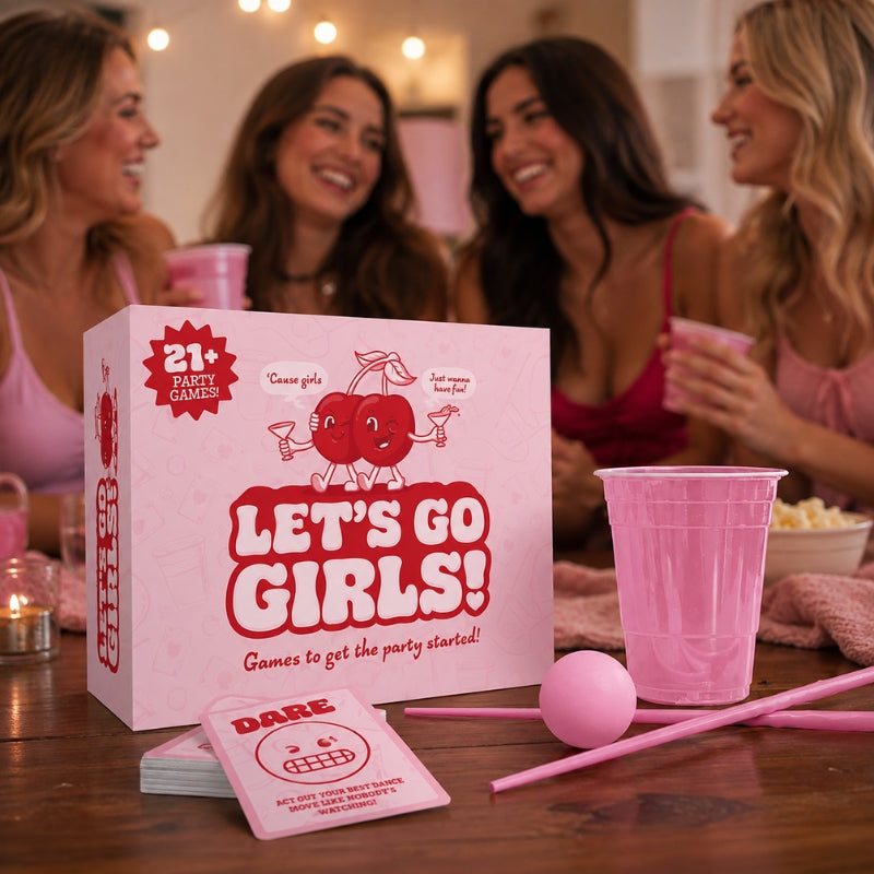 Bubblegum Stuff Let's Go Girls! on a wooden table with four women smiling in the background. The set includes a pink box labeled 'LET'S GO GIRLS!', pink cups, a pink ball, straws, and cards.