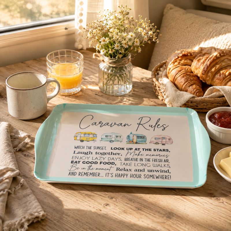 A Caravan Bamboo Melamine Serving Tray with rounded corners sits on a wooden table in a breakfast setting. The tray has a pale aqua border and a white center printed with the phrase 'Caravan Rules' in script, plus small illustrated campers and a short poem.