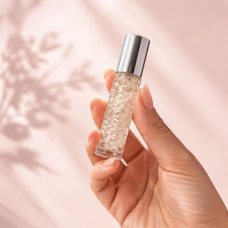 Hand holding a 10 ML Clarity essential roller a soft pink background
