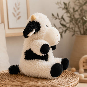Side view of Curly Cow Soft Toy White & Black 18cm plush toy on a woven basket in a nursery by Love Shack Giftware