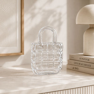 Clear glass bag on a light surface with books and a lamp in the background