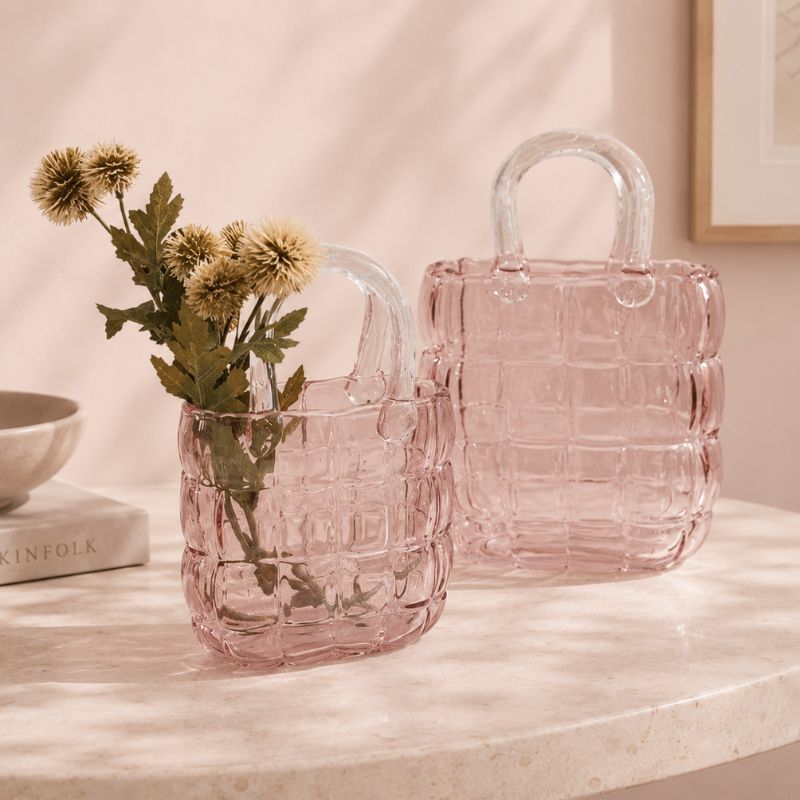 Pink textured handbag with a plant inside on a marble surface.