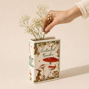 Hand placing flowers into a decorative tin with 'Enchanted Garden' design on a beige - background- Loveshack Giftware