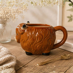 Highland Cow mug on a wooden surface with a spoon and books in the background.-Loveshack Giftware