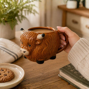 Person holding a Highland cow mug filled with a beverage on a wooden table.-Loveshack Giftware