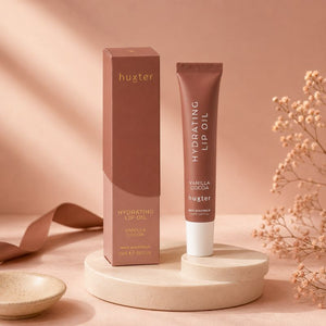 Huxter Hydrating Lip Oil Vanilla Cocoa with matching box on warm blush studio pedestal