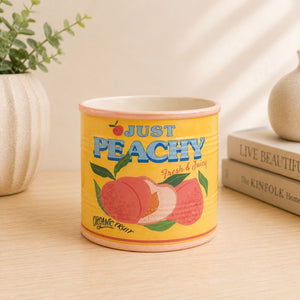 Yellow container with 'Just Peachy' text and peach illustrations on a wooden surface.