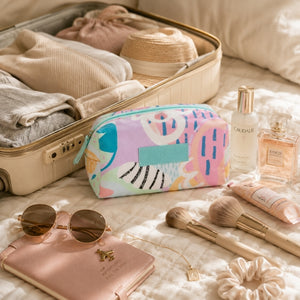Haven pastel makeup cosmetic bag beside an open suitcase with travel beauty essentials