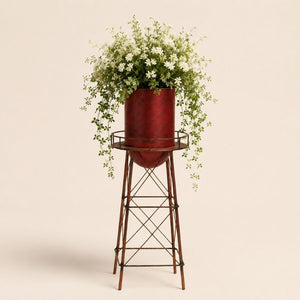Metal garden water tower planter with cascading white flowers on a light beige background.