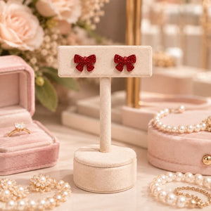Mini Bow Stud Earrings on a stand with jewelry and flowers in the background