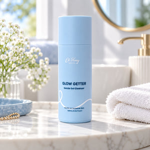 Oh Flossy Glow Getter Gentle Gel Cleanser 120ml in a pastel blue bottle on a bathroom vanity with white towels and flowers.