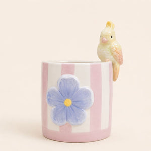 Ceramic mug with a blue flower design and a small bird figurine on a beige background