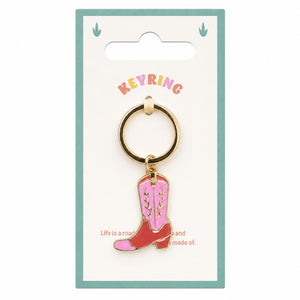 A Pink Cowboy Boot Enamel Keyring on a white card backing. The keyring features a gold-tone metal ring and a dangling charm shaped like a pink and red cowboy boot with white stitching, set against a white background with a teal border.