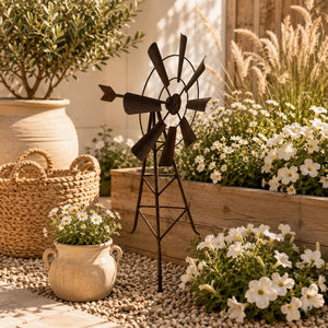 Rustic windmill garden stake styled beside a raised flower bed with woven baskets, white blooms, and natural garden accents.