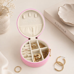 A Small Jewellery Case – Berry is shown open on a light cream surface, containing several rings and bracelets. The box has a pink exterior, cream interior, and small ring slots on the lid.