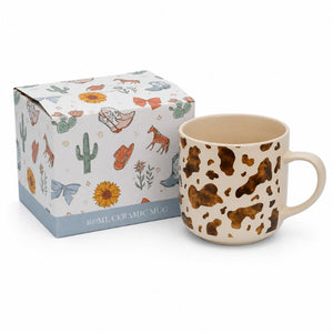 A 400ml Splosh - Saddle & Bloom Cow Mug on a cream background, shown next to its illustrated gift box on a white background.