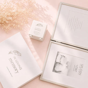 Album with 'A Moving Memory' text, photo of a woman, and small box on a pink surface.