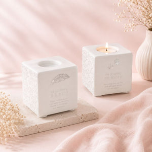 Two white textured candle holders with engraved text on a pink surface.