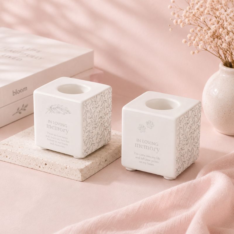 Two white textured candle holders on a pink surface with a blurred background
