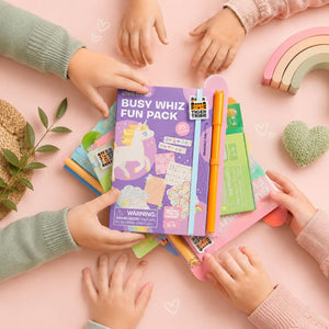 Children's hands around a Busy Whiz Fun Pack on a pink surface with toys and stationery items. - Loveshack Giftware