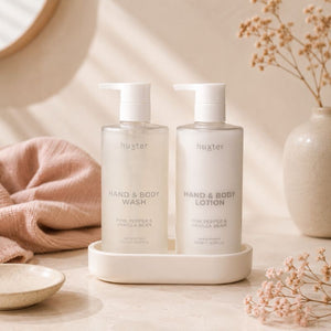 Huxter Pink Pepper & Vanilla Bean Hand and Body Wash and Lotion bottles styled in a warm neutral bathroom setting