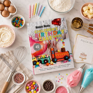 Children's Birthday Cake Book surrounded by baking tools, cake decorations, sprinkles, recipe cards, and birthday candles.