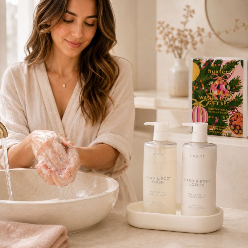 Woman applying Huxter Pink Pepper & Vanilla Bean body lotion beside matching wash and lotion bottles