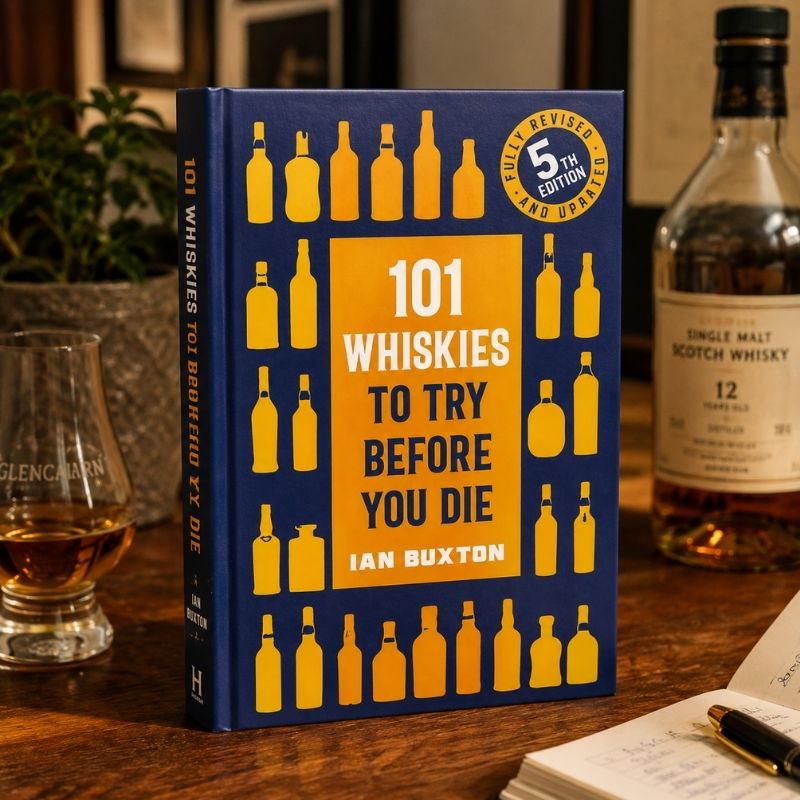 Book titled '101 Whiskies to Try Before You Die' by Ian Buxton on a wooden surface with a glass of whiskey and a bottle in the background.