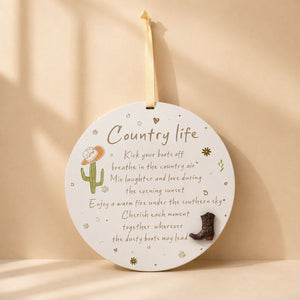 Country Life round hanging plaque with cowboy boot accent and cactus illustration on a warm beige background.