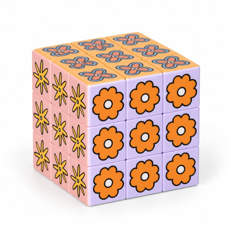 A 3x3x3 Art Cube – Flower Pop puzzle cube with a retro floral pattern, featuring orange flowers on the front, yellow flowers on the left, and a purple top with orange and blue geometric designs, set against a plain white background.