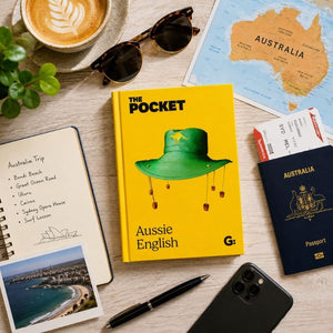 Pocket Aussie English book surrounded by Australian travel essentials including passport, map, notebook, and coffee