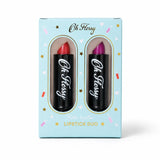 Oh Flossy Lipstick Duo in a light blue gift box with two black lipstick tubes visible through oval cutouts. One lipstick bullet is red and the other is purple, with the brand name 'Oh Fessy' printed on both tubes.
