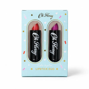 Oh Flossy Lipstick Duo in a light blue gift box with two black lipstick tubes visible through oval cutouts. One lipstick bullet is red and the other is purple, with the brand name 'Oh Fessy' printed on both tubes.