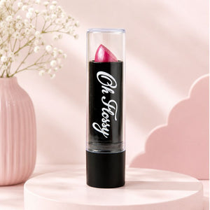 A pink Oh Flossy lipstick bullet in a clear tube with a black base, standing upright on a round pink pedestal. The tube has the words 'Oh, Flossy' in white script.