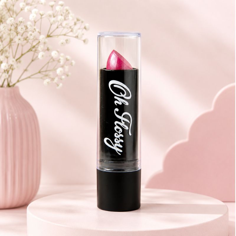 A pink Oh Flossy lipstick bullet in a clear tube with a black base, standing upright on a round pink pedestal. The tube has the words 'Oh, Flossy' in white script.