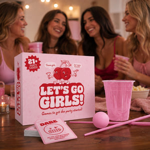 Bubblegum Stuff Let's Go Girls! on a wooden table with four women smiling in the background. The set includes a pink box labeled 'LET'S GO GIRLS!', pink cups, a pink ball, straws, and cards.
