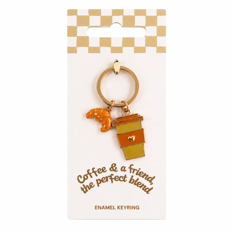 An enamel keyring charm featuring a small orange croissant and a coffee cup with the text 'Coffee & a friend, the perfect blend' on a white display card.