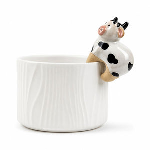 A white ceramic cup with a textured vertical wavy pattern, featuring a small 3D cow figurine perched on the rim. The cow is white with black spots, pink ears and nose, and tan legs, set against a plain white background.-Cow Pot Hanger - 8cm