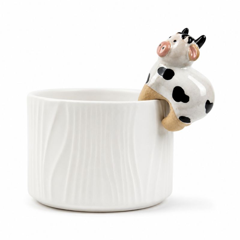 A white ceramic cup with a textured vertical wavy pattern, featuring a small 3D cow figurine perched on the rim. The cow is white with black spots, pink ears and nose, and tan legs, set against a plain white background.-Cow Pot Hanger - 8cm