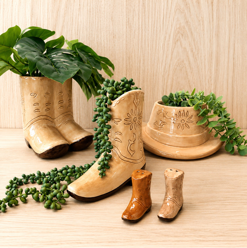 Western-inspired tan ceramic boot and hat planters with trailing greenery on a light wooden surface