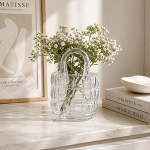 Clear glass vase with flowers on a shelf next to books and a framed picture.