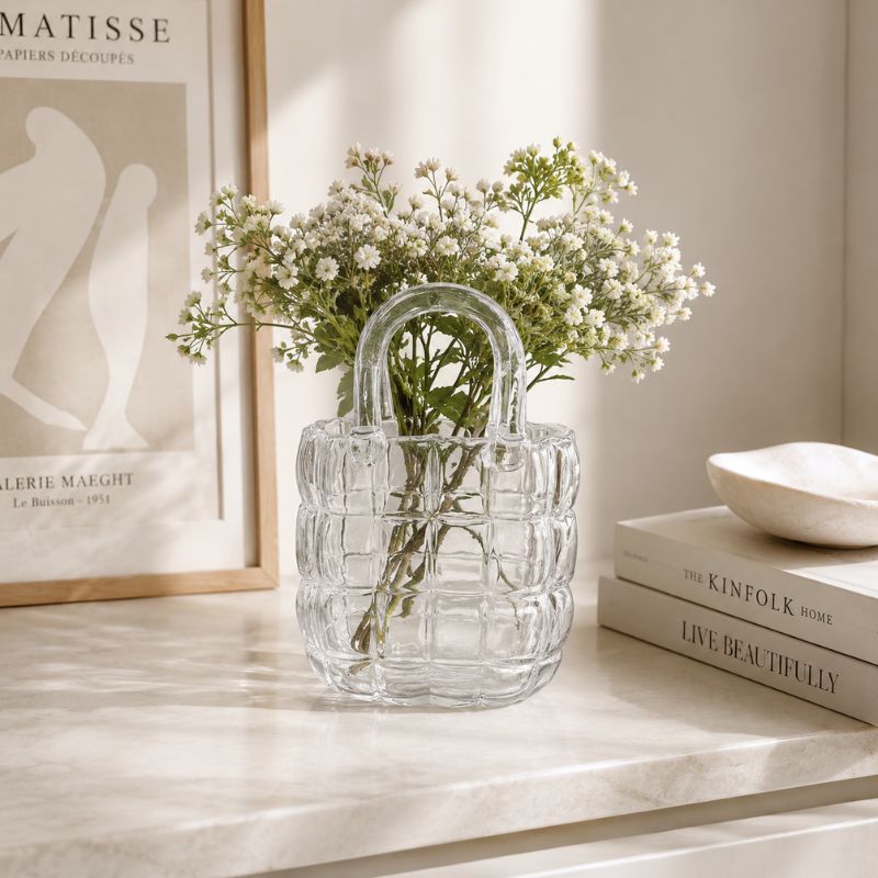 Clear glass vase with flowers on a shelf next to books and a framed picture.