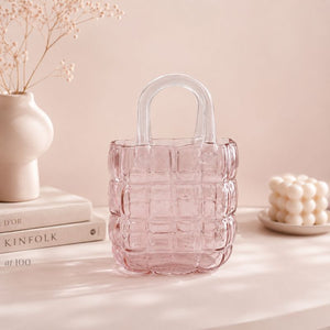 Pink textured glass vase on a table with books and decorative items.