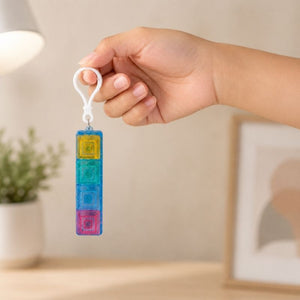 Hand holding a Fidget Fingers Keyboard Click Keychain with a blurred indoor background