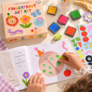 A child's fingerprint art kit shown in use, with an open activity book featuring a ladybug design, colorful fingerprint ink pads, stickers, and the product box on a light tabletop.