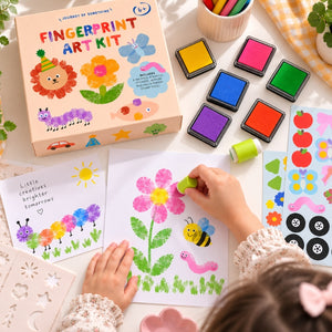 A child's hands are shown using a fingerprint art kit on a white surface, with the colorful product box, fingerprint stamps, stickers, and art supplies arranged around them. The box reads 'FINGERPRINT ART KIT' and shows playful animal and flower illustrations.