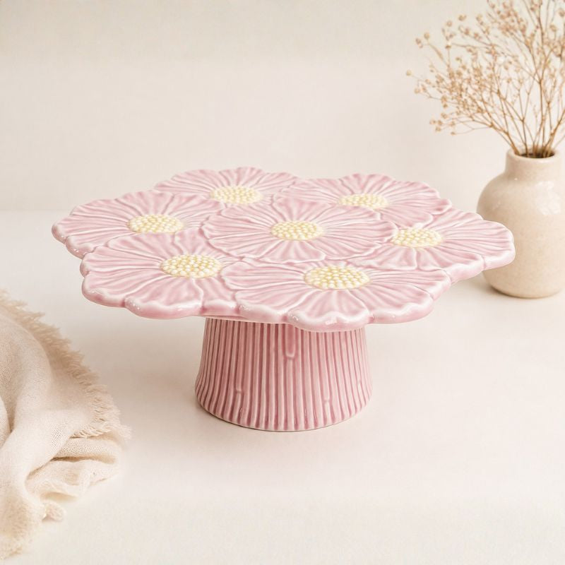 Pink floral cake stand on a light surface with a vase in the background