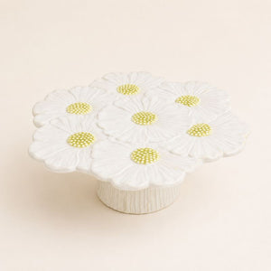 White ceramic flower cake stand with daisy patterns on a beige background