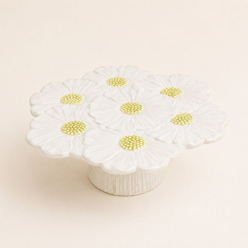 White ceramic flower cake stand with daisy patterns on a beige background