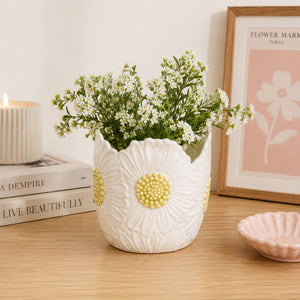 White floral-patterned vase with greenery on a wooden surface with books and a candle.